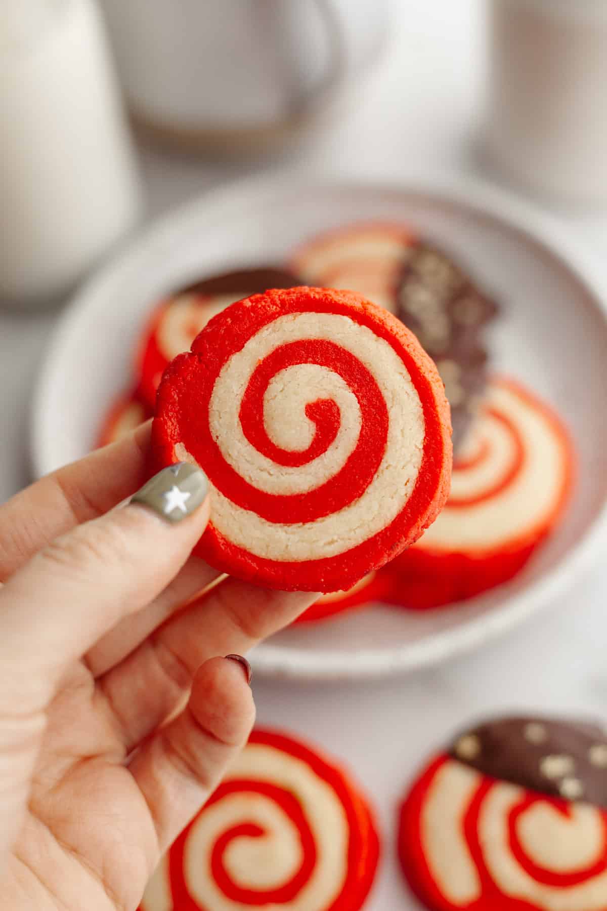 A hand holding a red and beige pinwheel cookie.