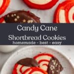 Red and white pinwheel candy cane shortbread cookies on a small plate, some of the cookies have been half dipped in chocolate.