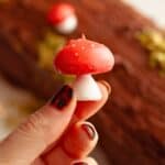 A hand holding a small meringue mushroom with a red cap and white stalk.