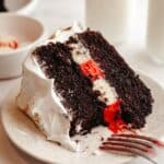 A slice of peppermint bark cake with white frosting on a plate.