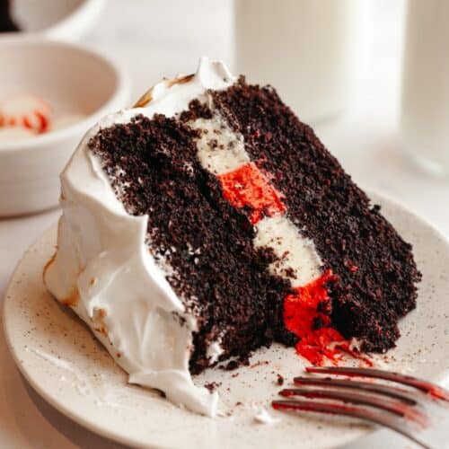 A slice of peppermint bark cake with white frosting on a plate.