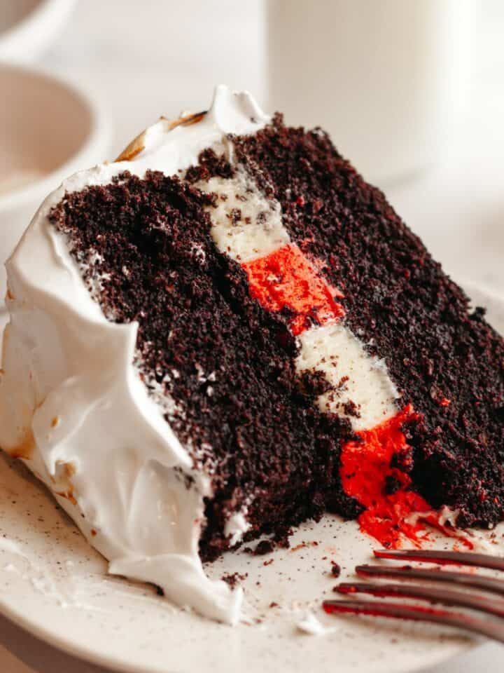 A slice of peppermint bark cake with white frosting on a plate.