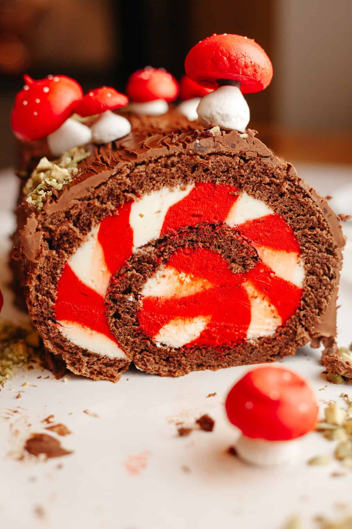 A chocolate yule log with white and red striped filling, decorated with meringue mushrooms on a white platter.