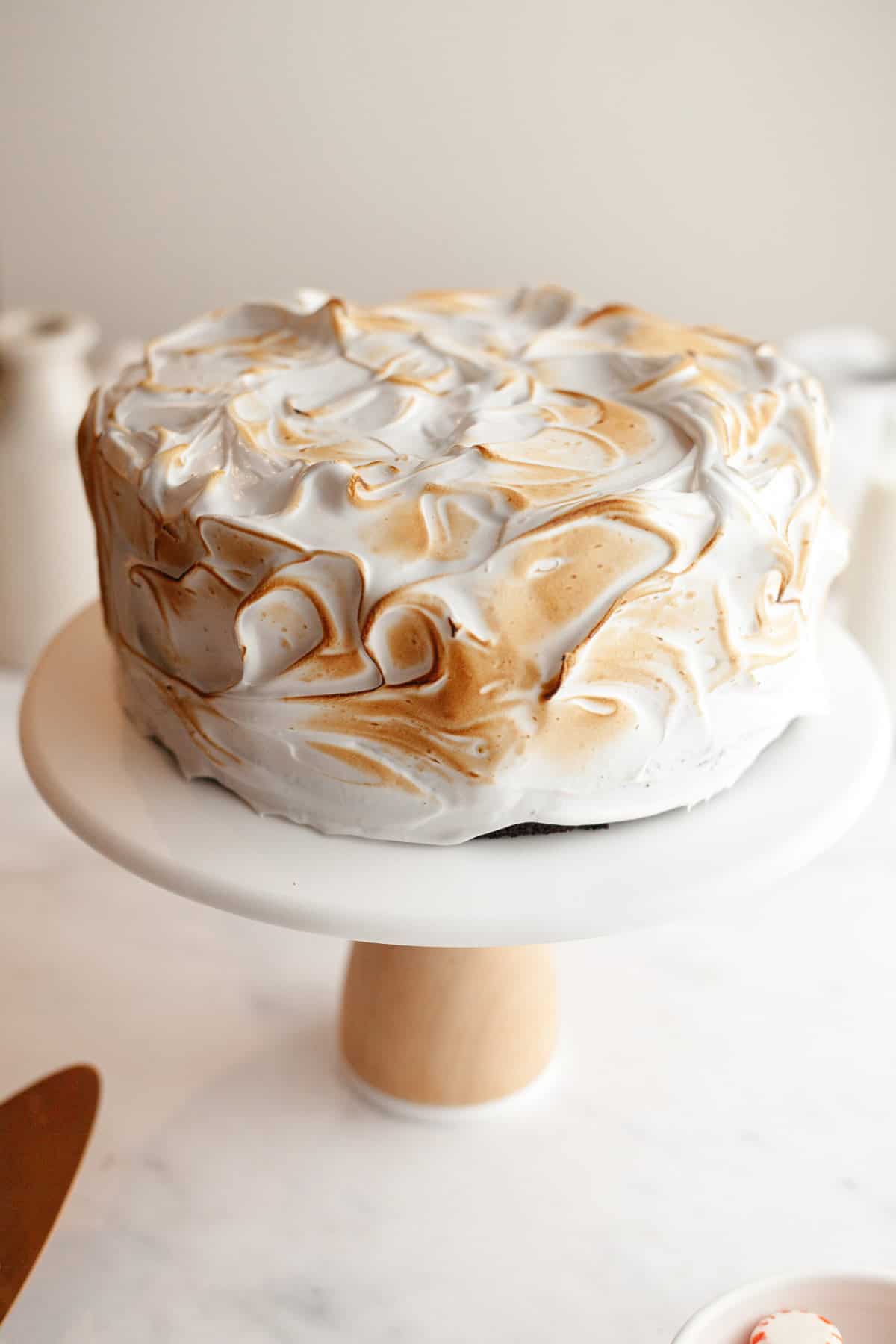 A toasted marshmallow cake on a white cake stand.