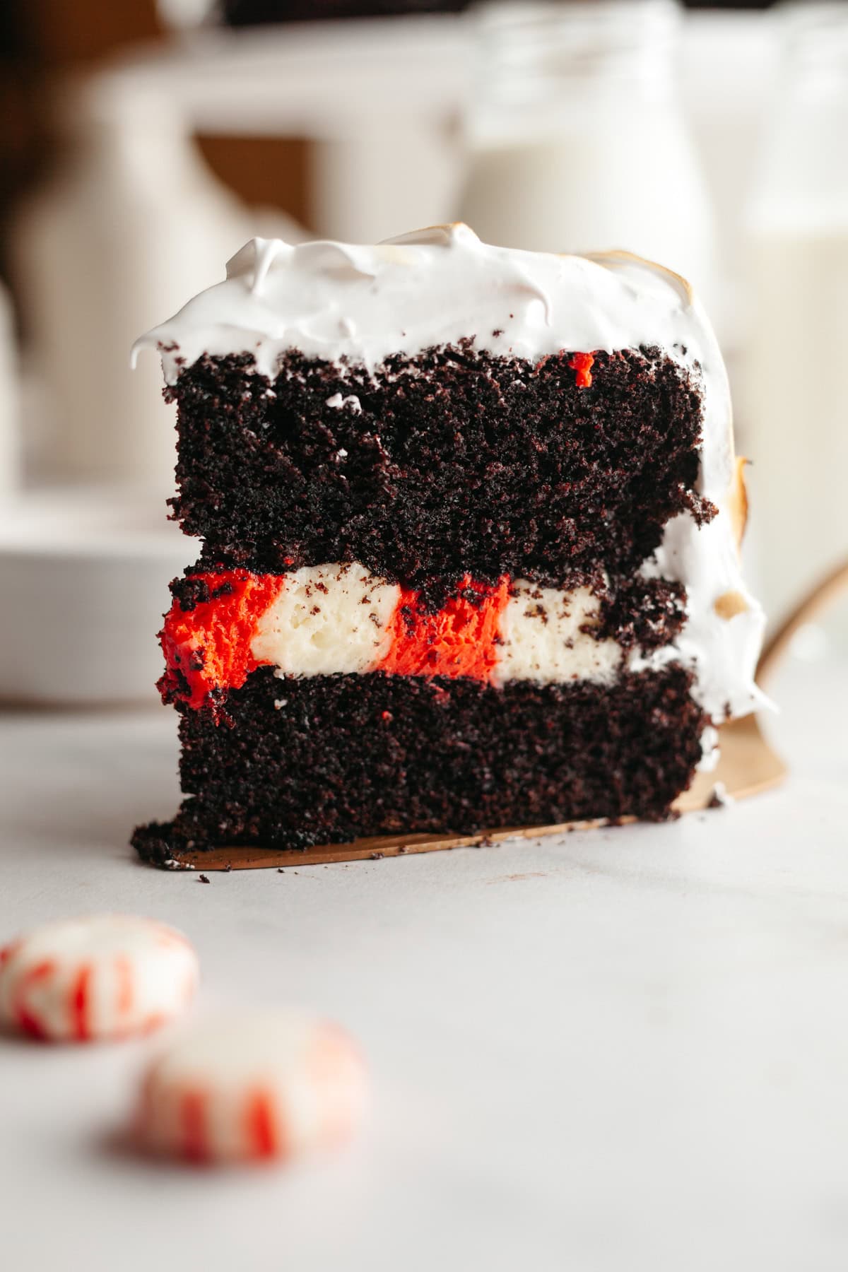 A slice of peppermint bark cake with white frosting on a gold cake server.