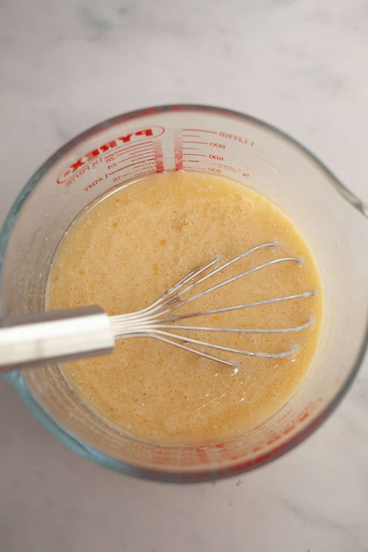A glass jug with a whisk and yellow cake batter.