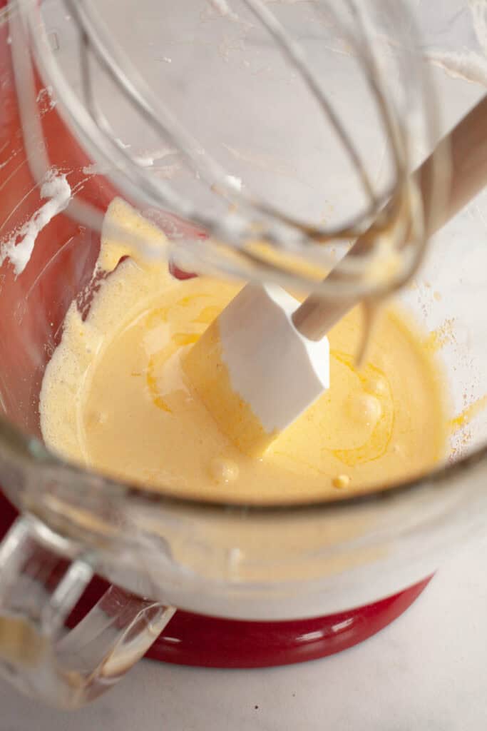 A red stand mixer with glass bowl with a pale yellow mixture in it.