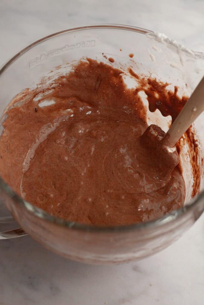 A glass mixing bowl with a chocolate cake batter.