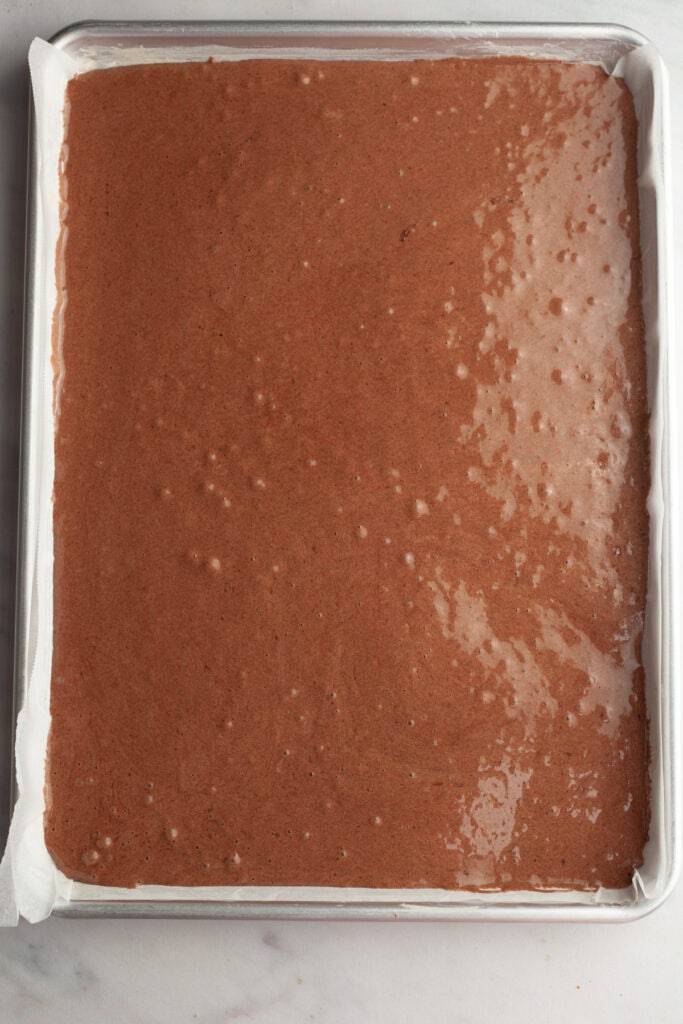A large rectangular sheet pan with unbaked chocolate cake batter in it.