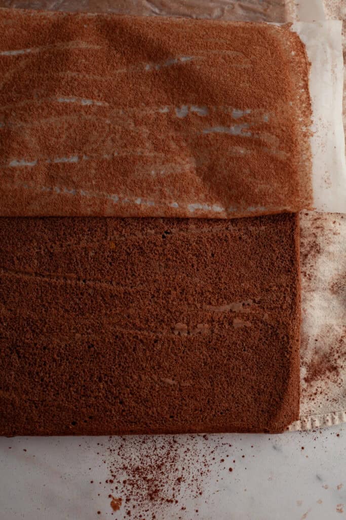 A rectangular chocolate cake with parchment paper being peeled off of it.