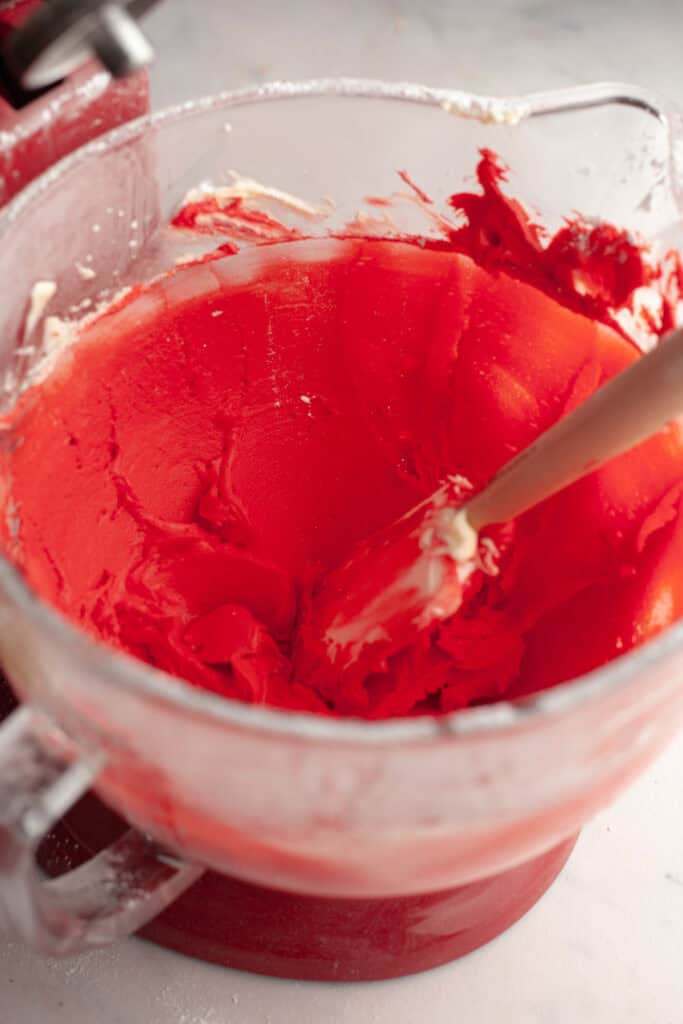 A stand mixer bowl with red frosting in it.