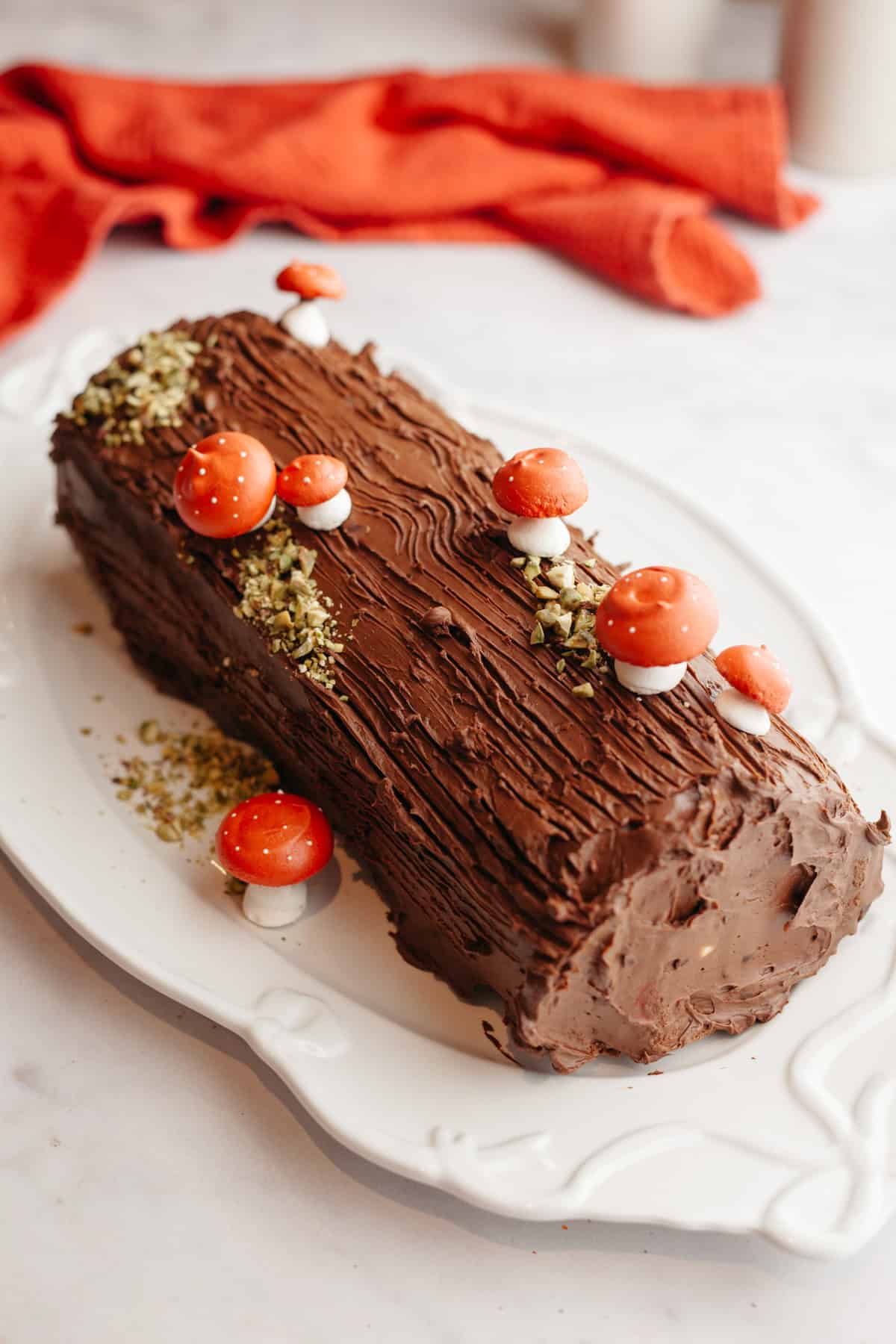 A chocolate yule log topped with meringue mushrooms on a white platter.