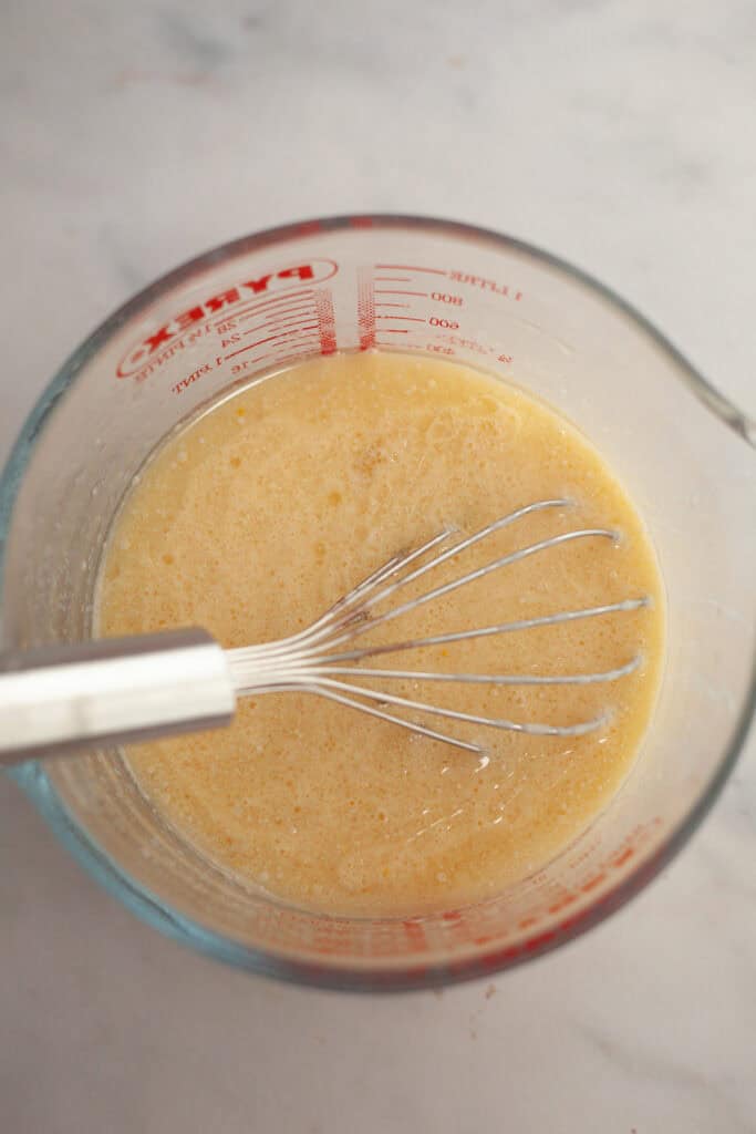 A glass jug with a whisk and yellow cake batter.