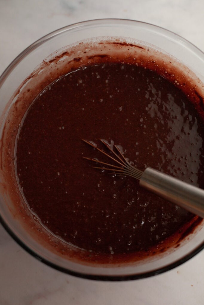 Chocolate cake batter in a glass bowl with a whisk.