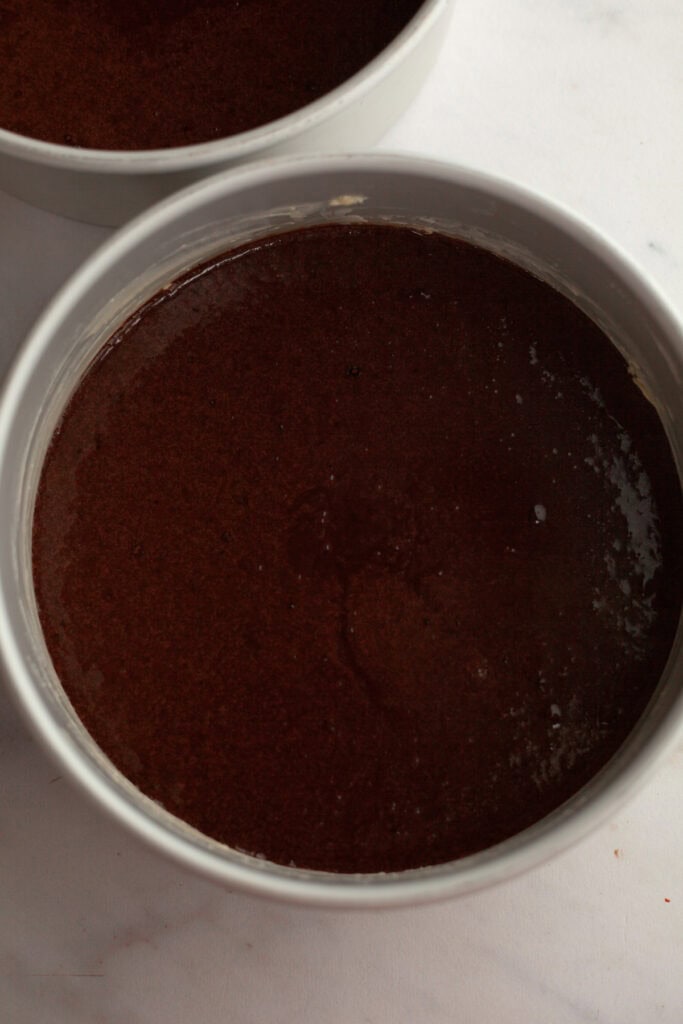Two cake pans with unbaked chocolate cakes in it.