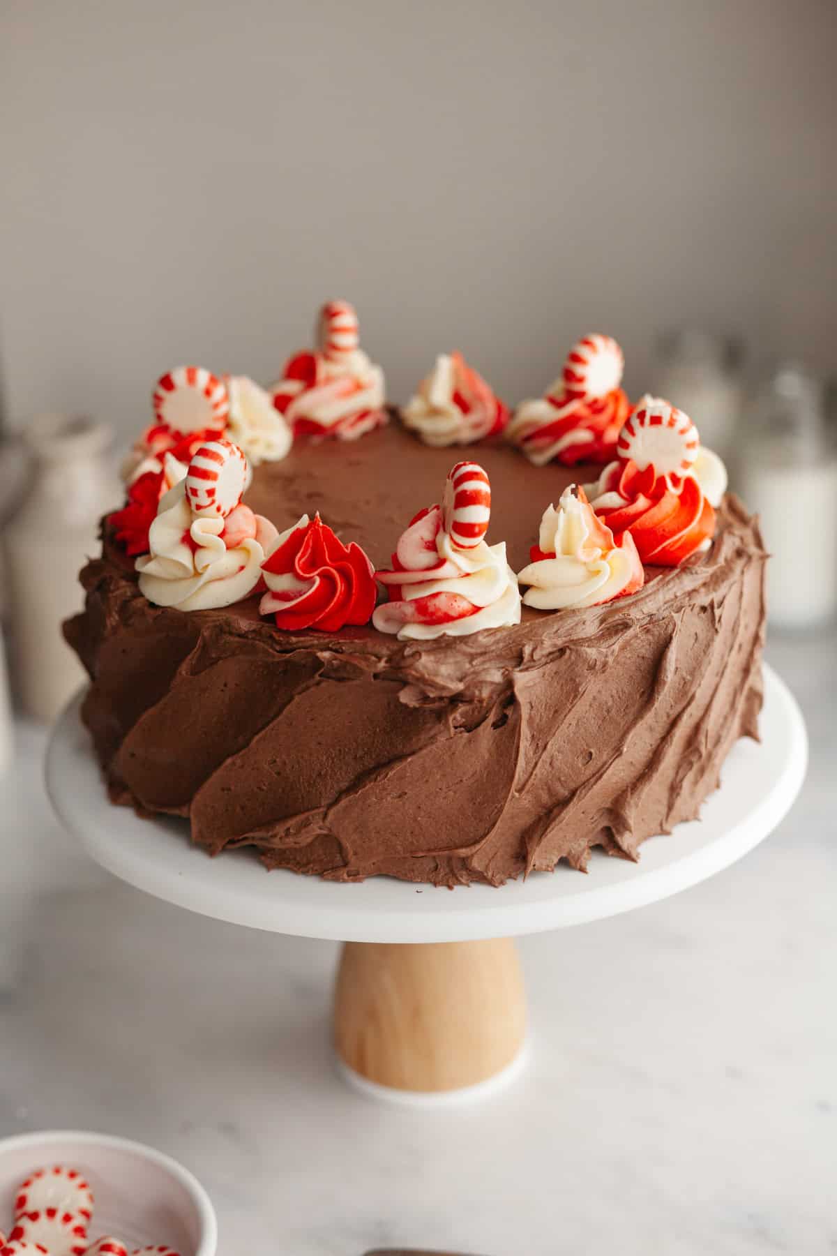 A chocolate frosted cake with candy cane swirled frosting on top, on a white cake stand.