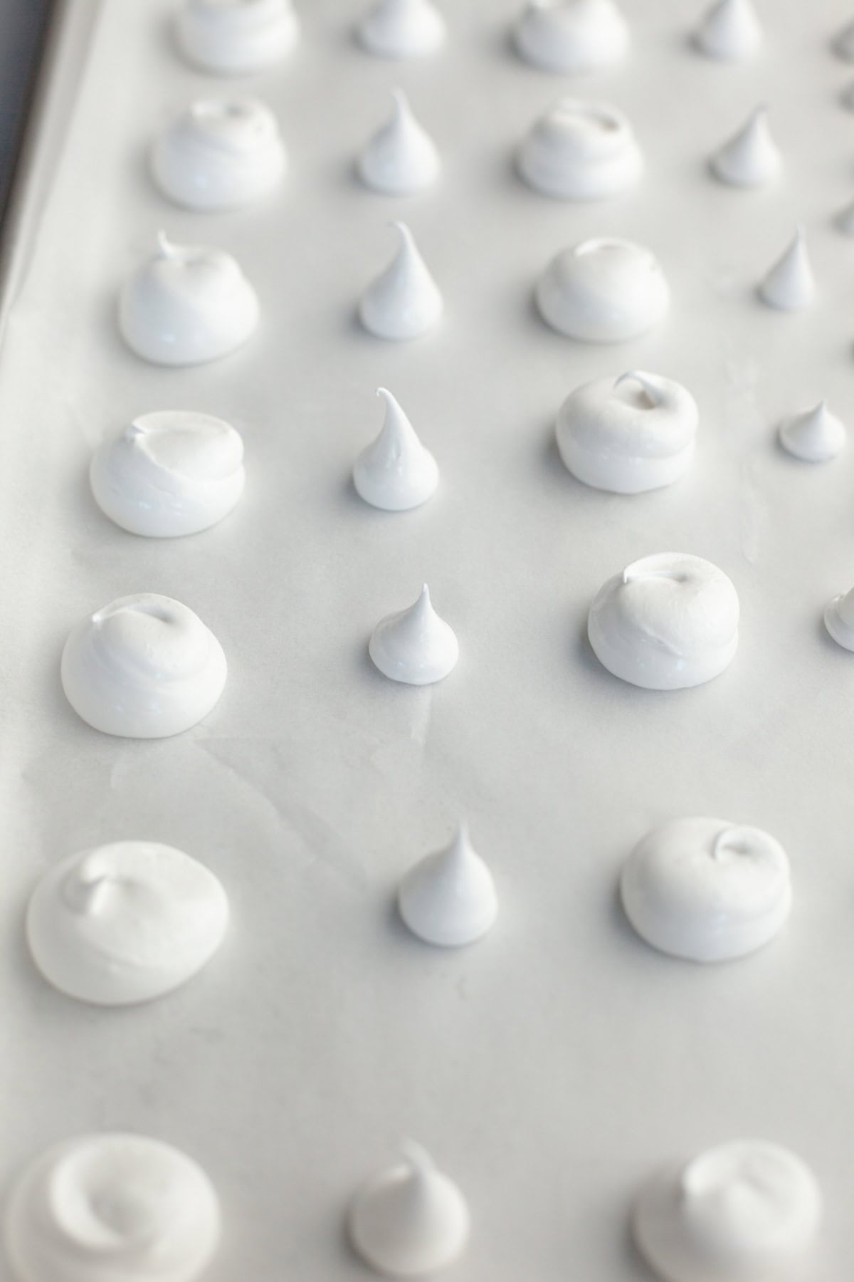 A parchment lined baking sheet with piped out meringue mushroom tops and stalks.