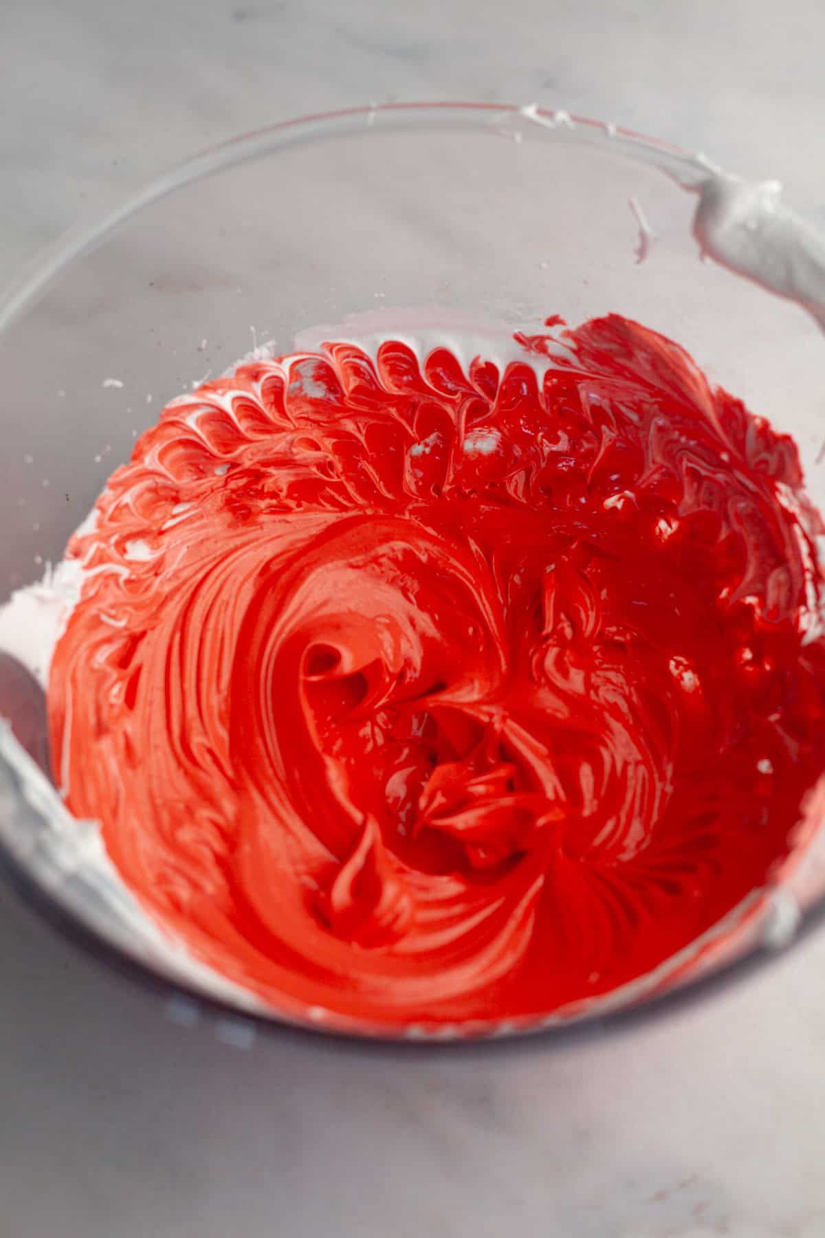 Red glossy meringue batter in a glass bowl.