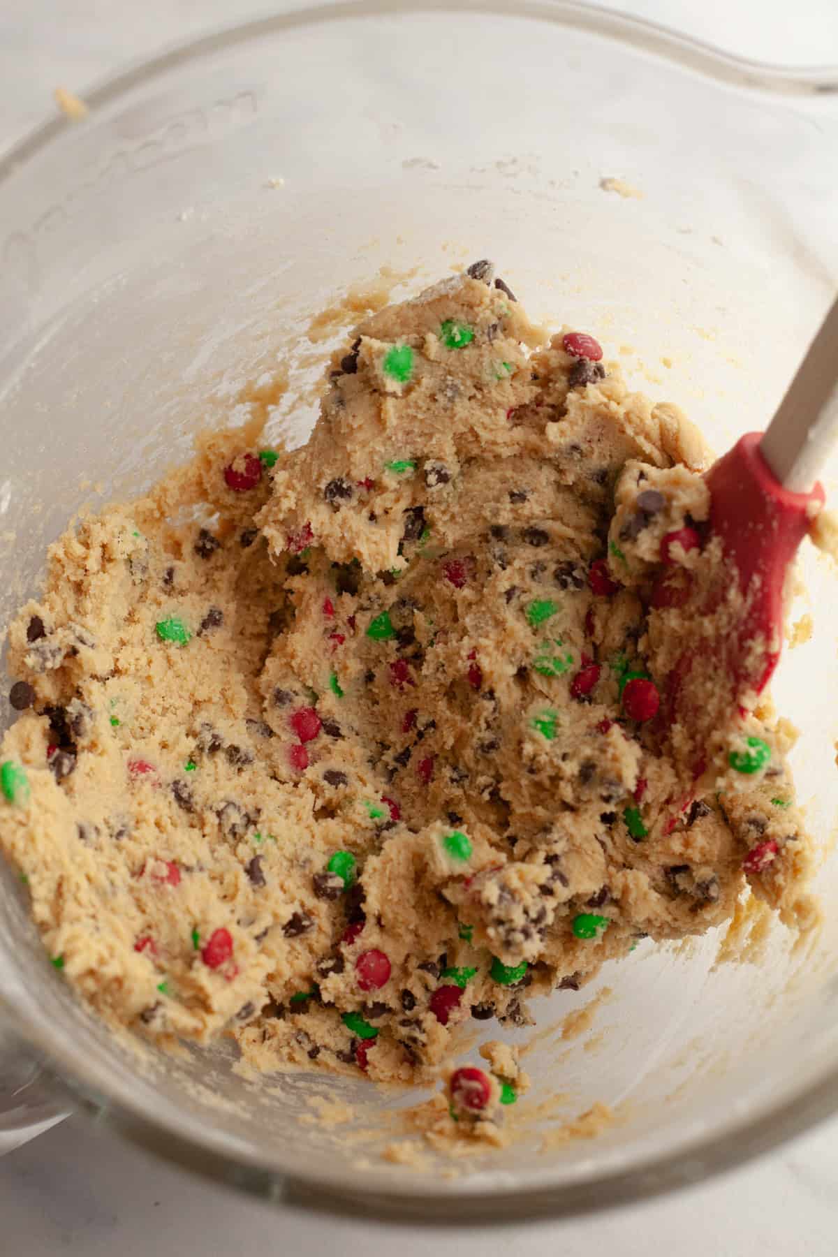 Chocolate chip and M&M cookie dough in a glass bowl.