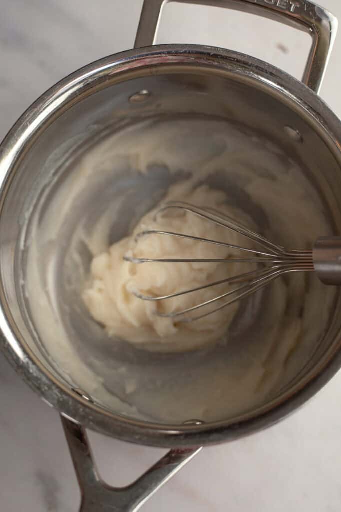 A silver saucepan with dough in it and a whisk.
