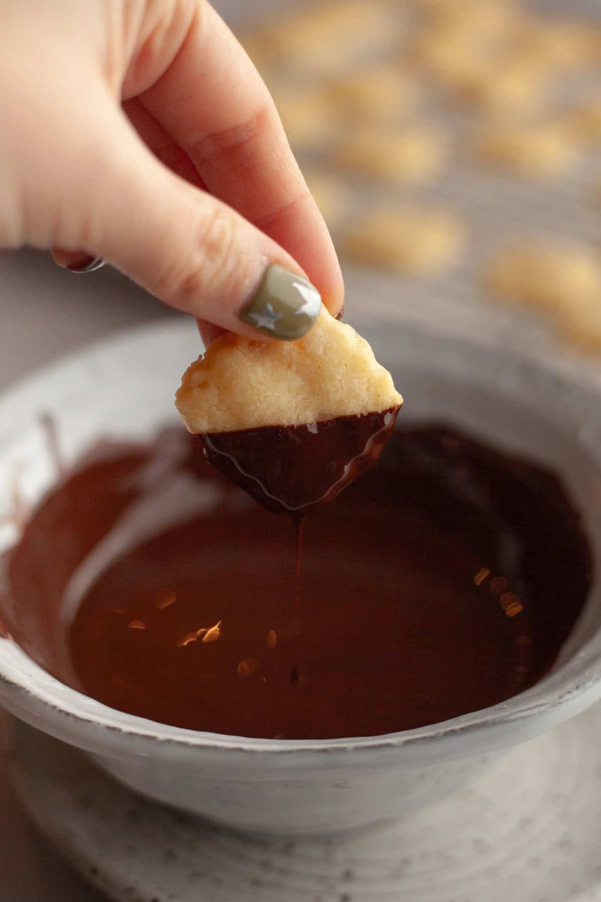 A hand dipping a shortbread cookie in melted chocolate.
