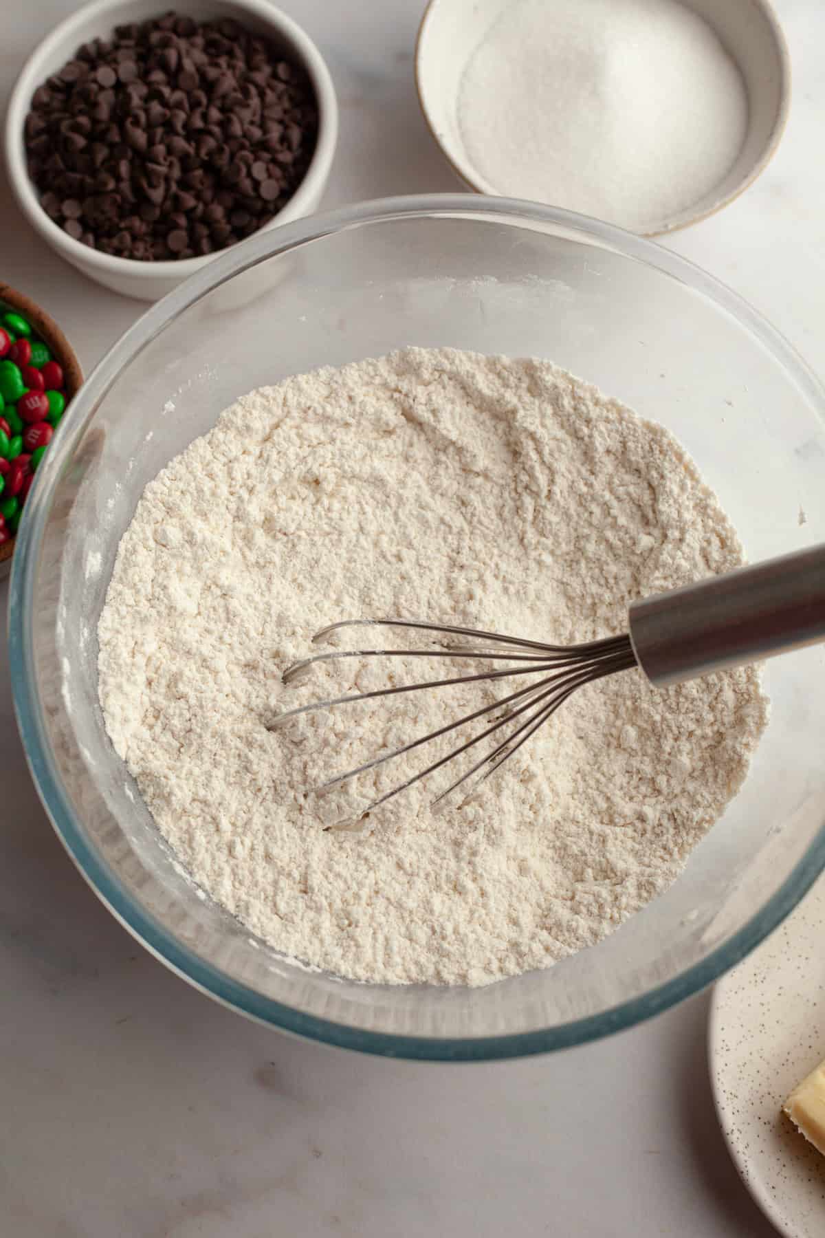 A glass bowl with flour and a whisk.