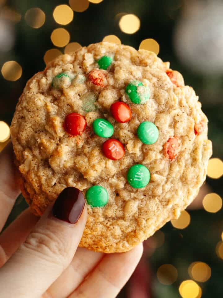 A hand holding an oatmeal cookie with red and green M&Ms.