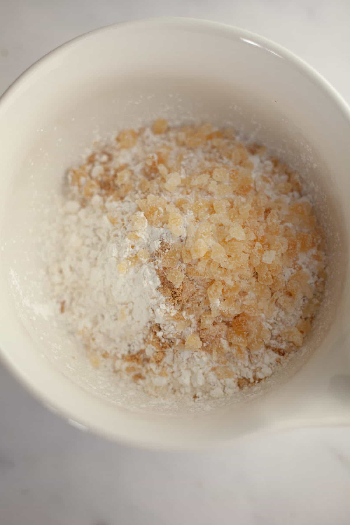 A white bowl with flour and chopped crystallized ginger.