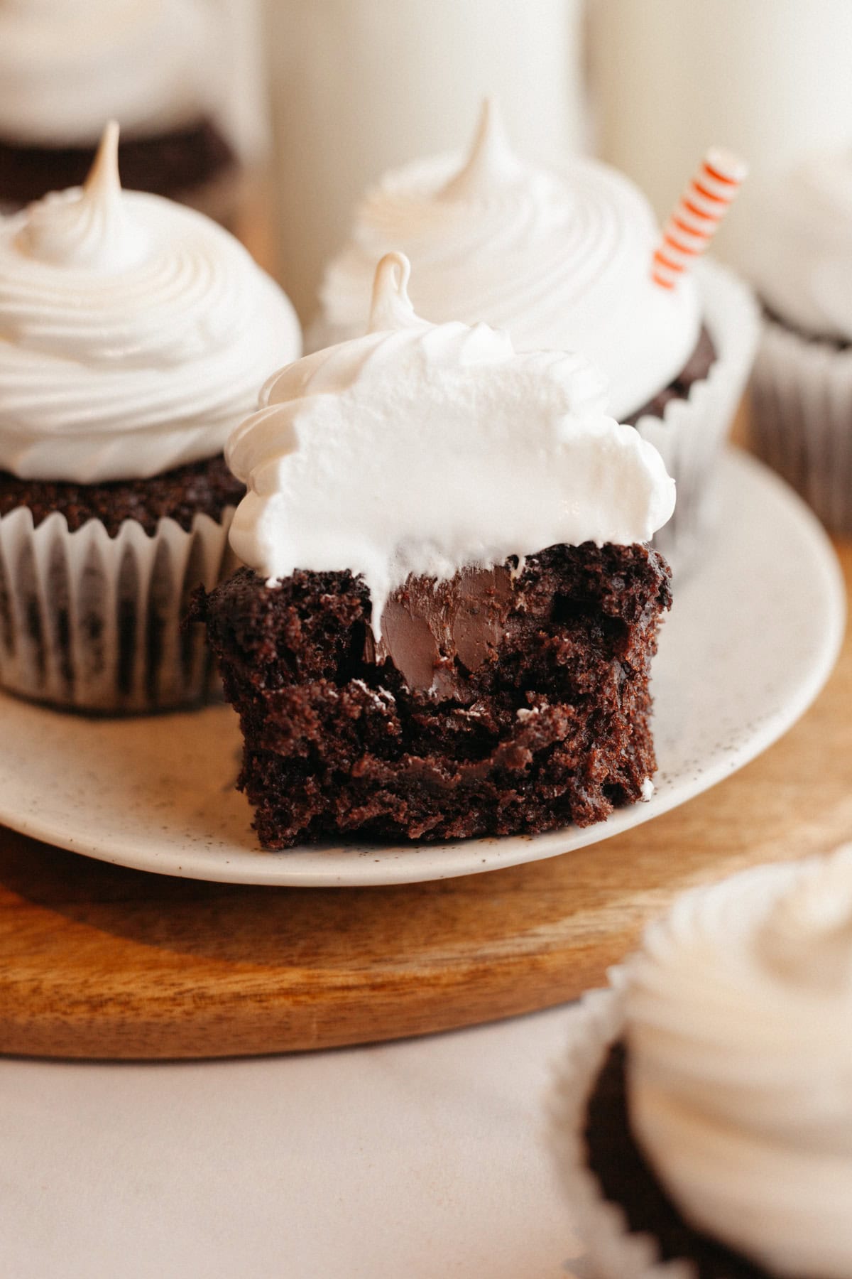 Chocolate cupcakes with toasted marshmallow frosting, one has a bite taken out of it to show a ganache filling.