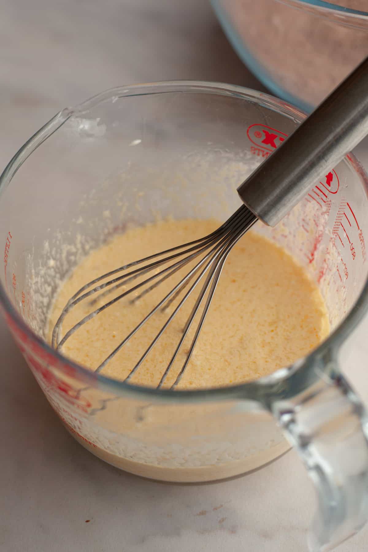 A glass jug with a yellow batter in it and a whisk.