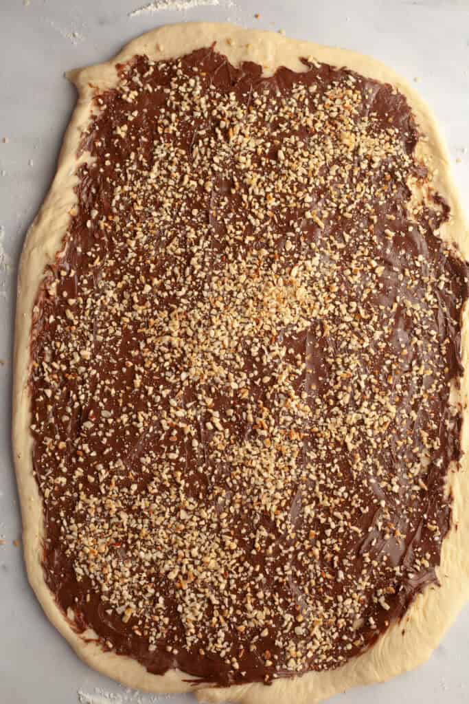 Rectangular dough covered in Nutella and chopped hazelnuts.