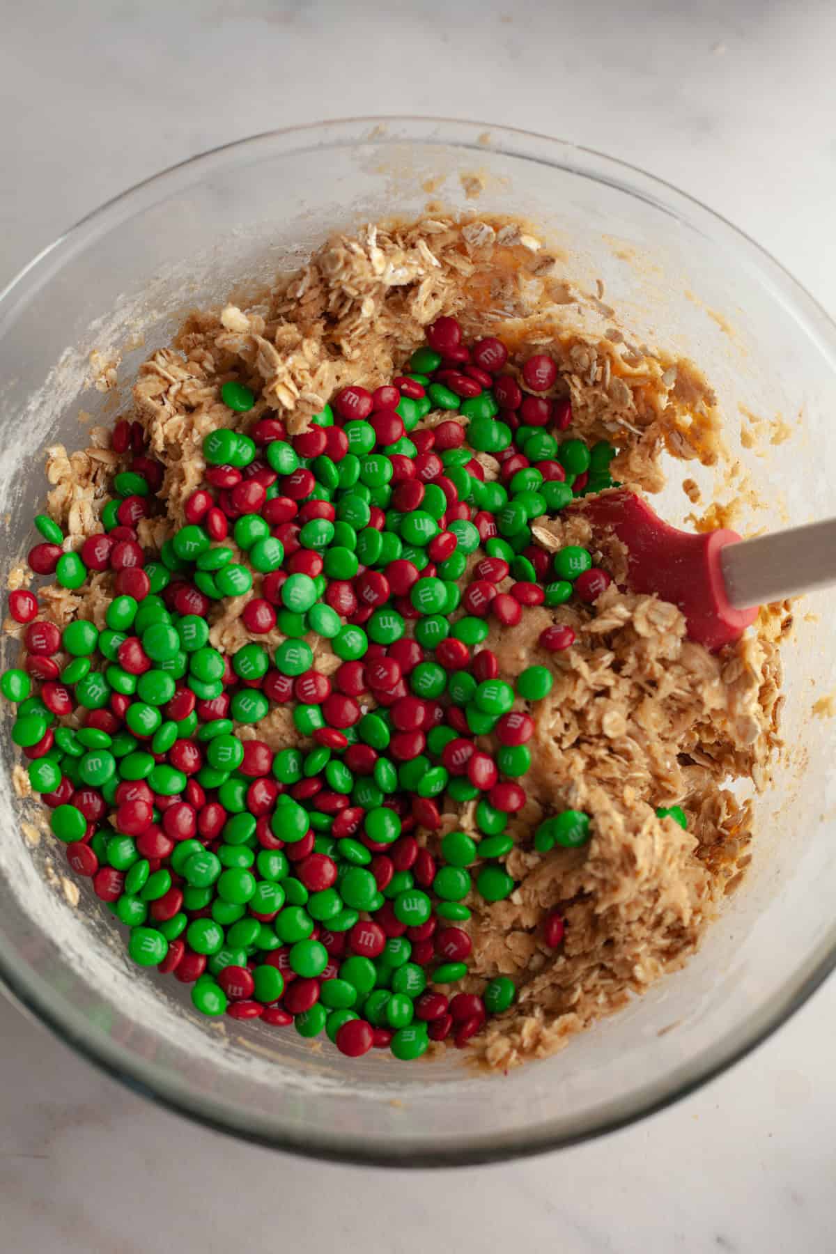 Oatmeal cookie dough in a bowl with red and green M&Ms.