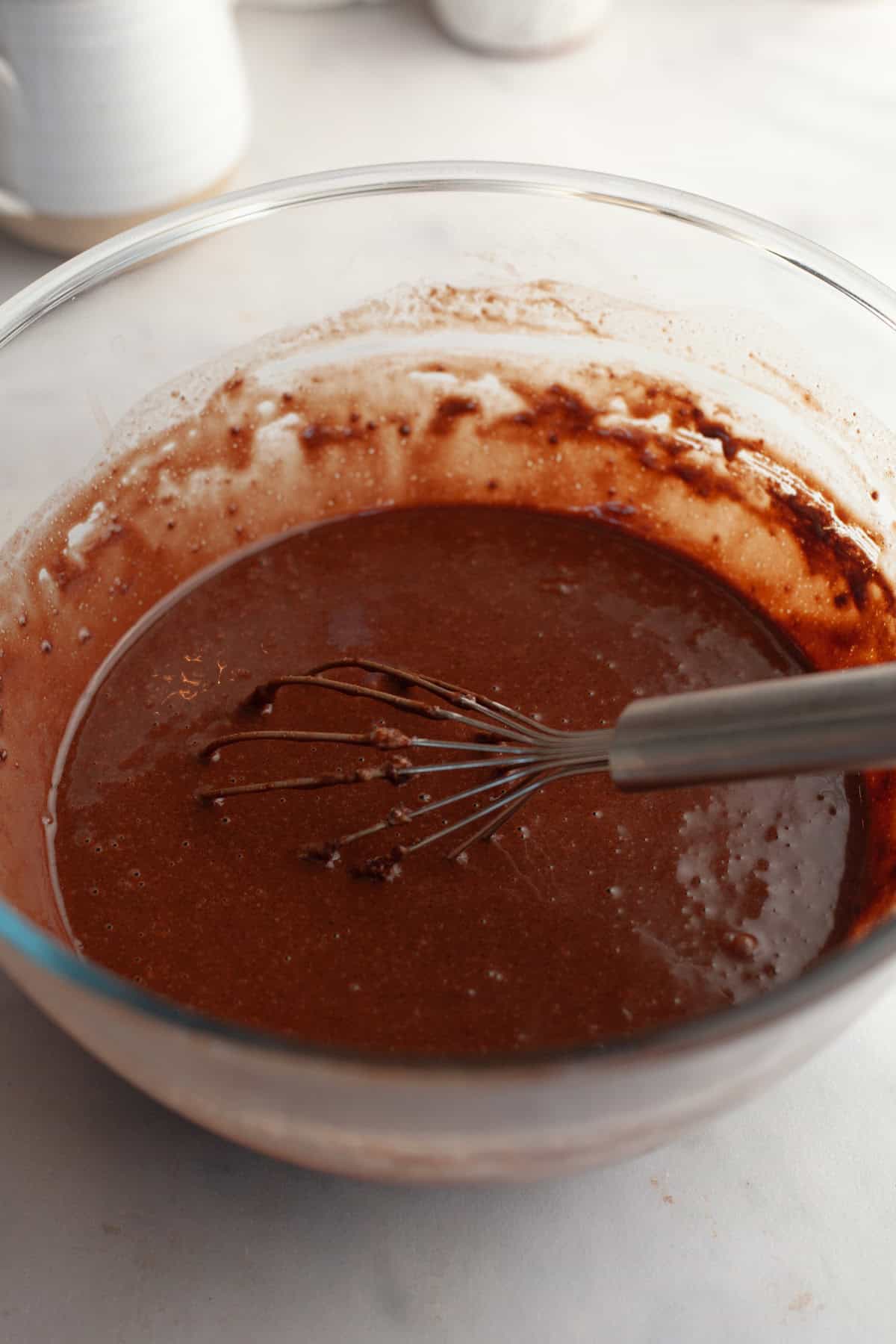 Chocolate cupcake batter in a glass bowl with a whisk.