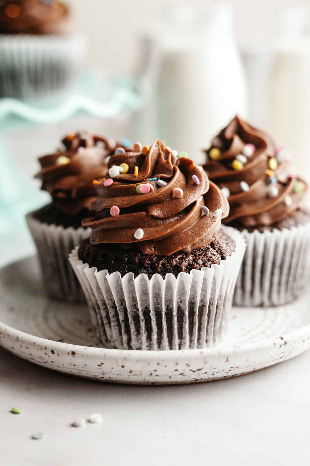 Three chocolate cupcakes with chocolate icing on a small plate.