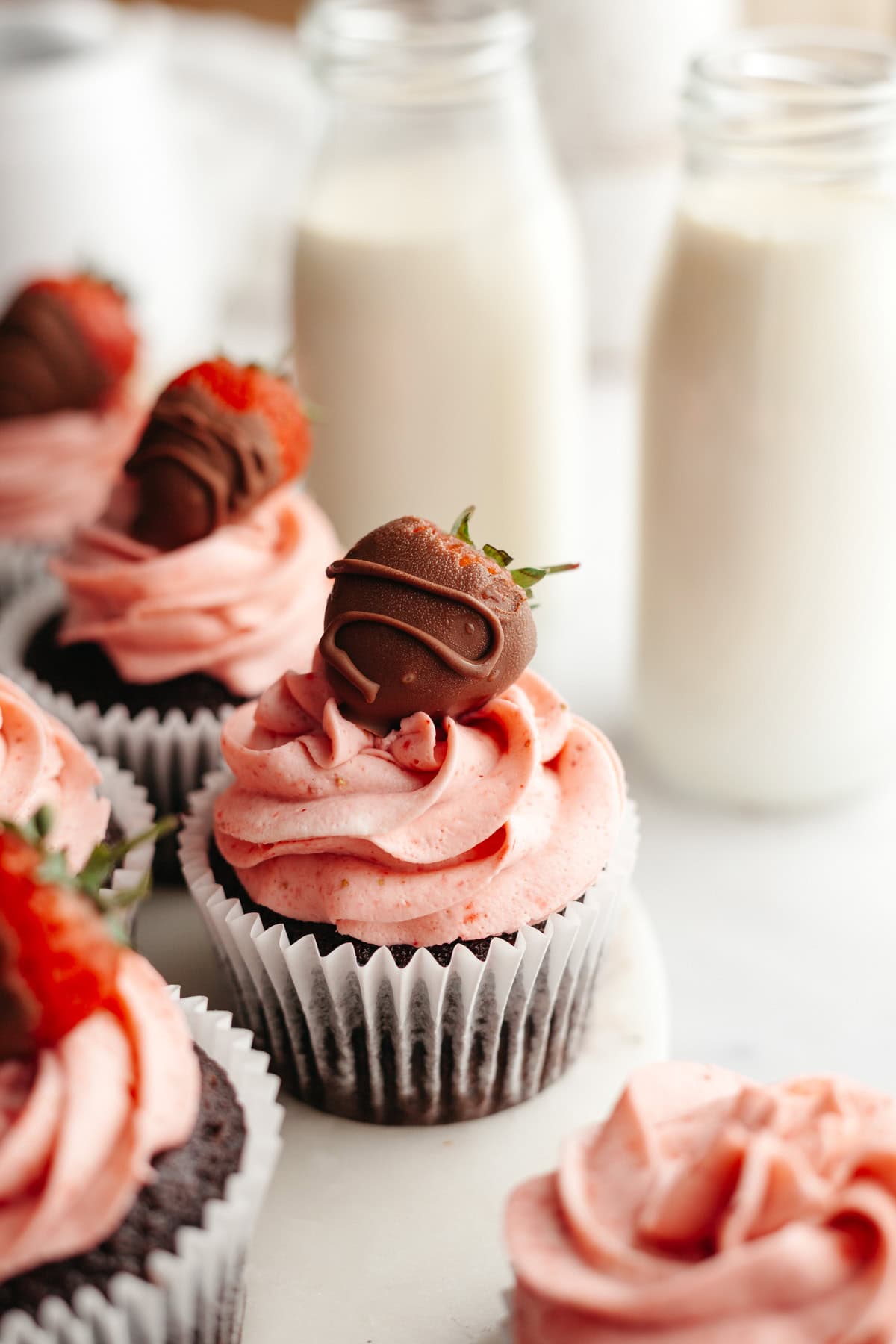A close up of strawberry frosted chocolate cupcakes, some have been topped with a chocolate covered strawberry.