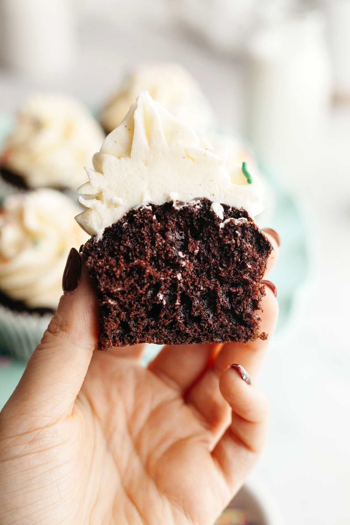 A hand holding a chocolate cupcake that's been cut in half.