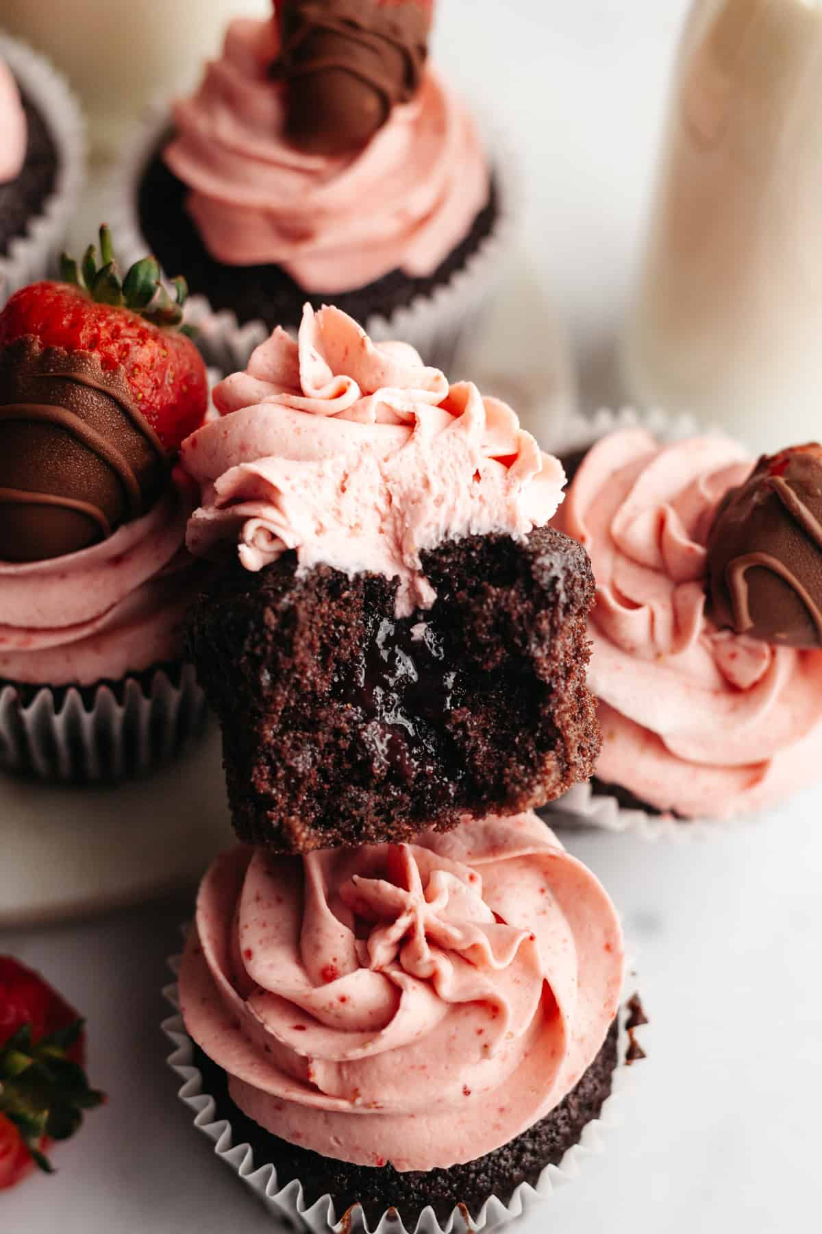 A close up of a chocolate cupcake with strawberry frosting with a bite taken out of it, showing a jam filled center.