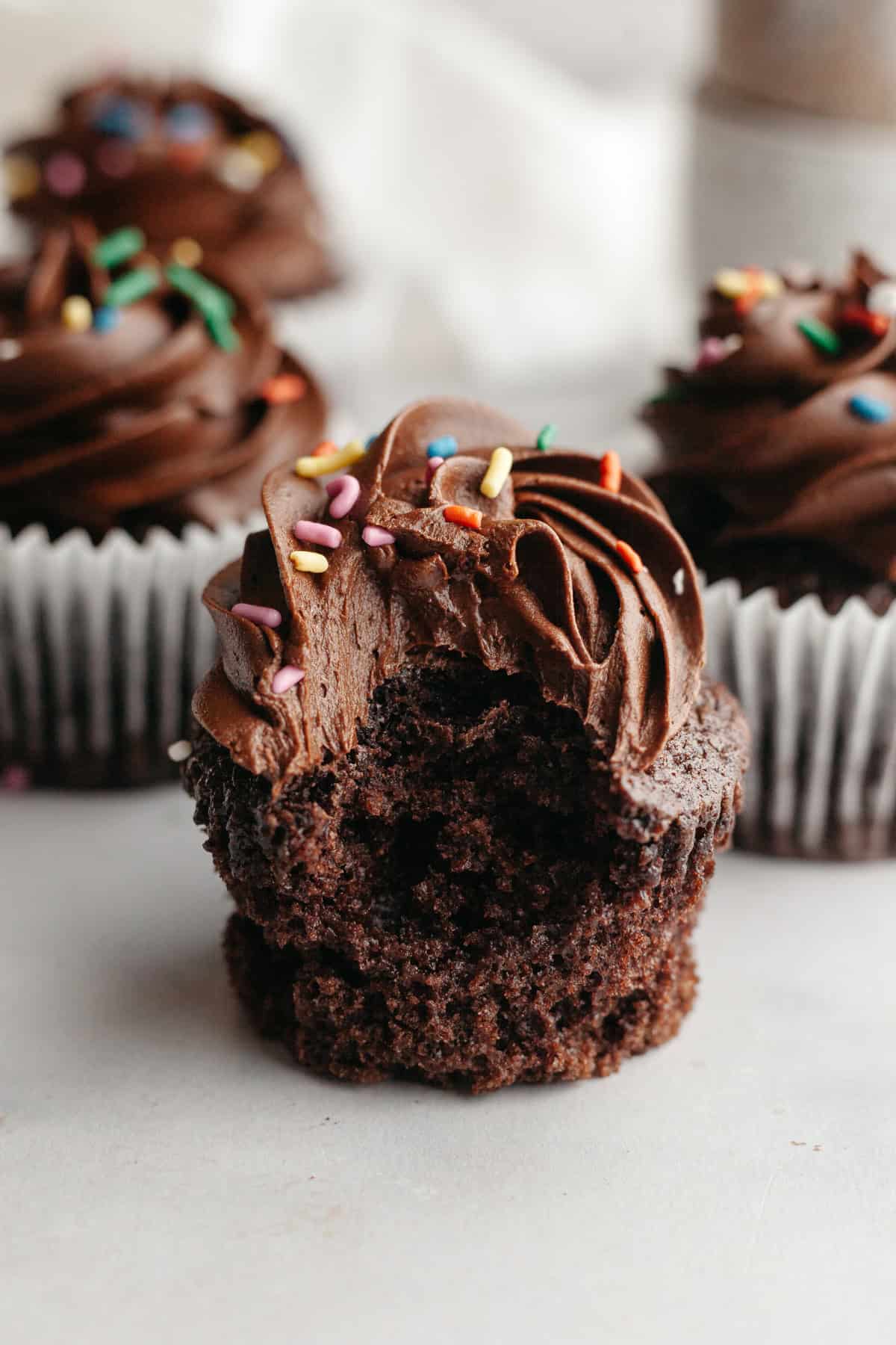 A chocolate cupcake with chocolate frosting with a bite taken out of it.