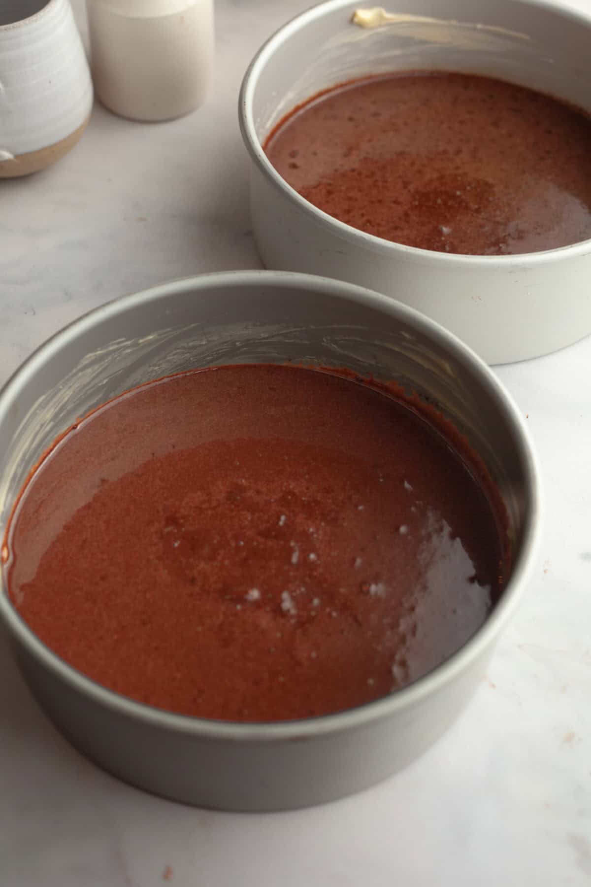Two cake pans with unbaked chocolate cake batter.
