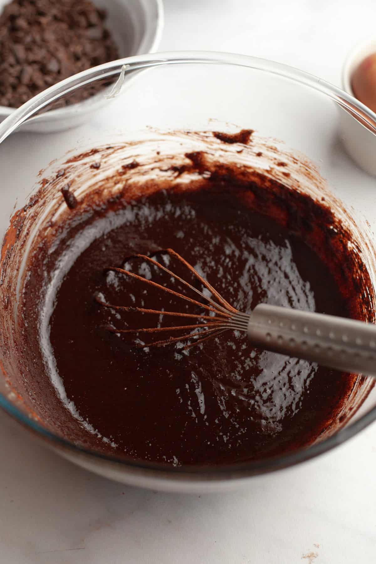 Brownie batter in a glass bowl with a whisk.