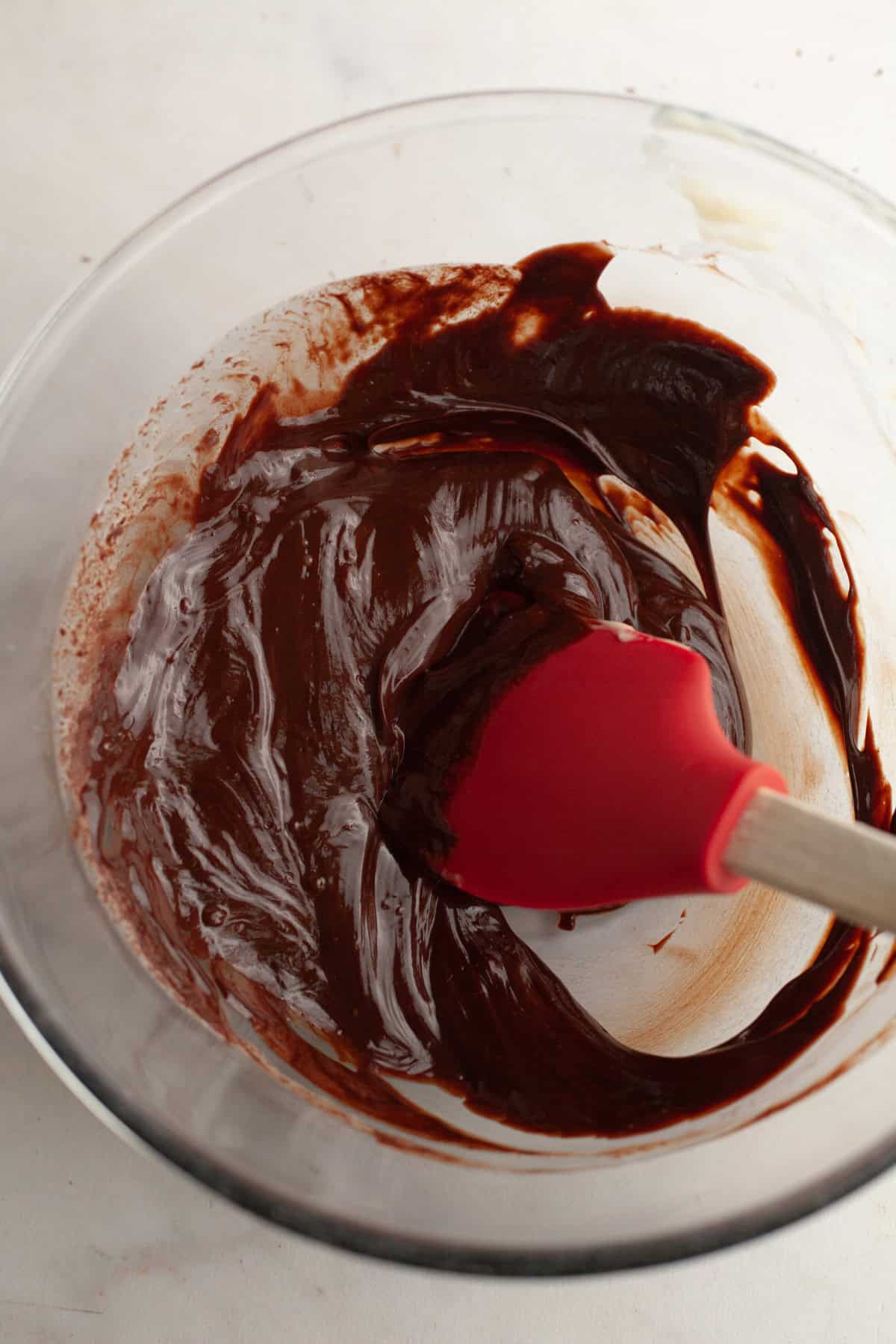 Chocolate ganache in a glass bowl with a red rubber spatula.
