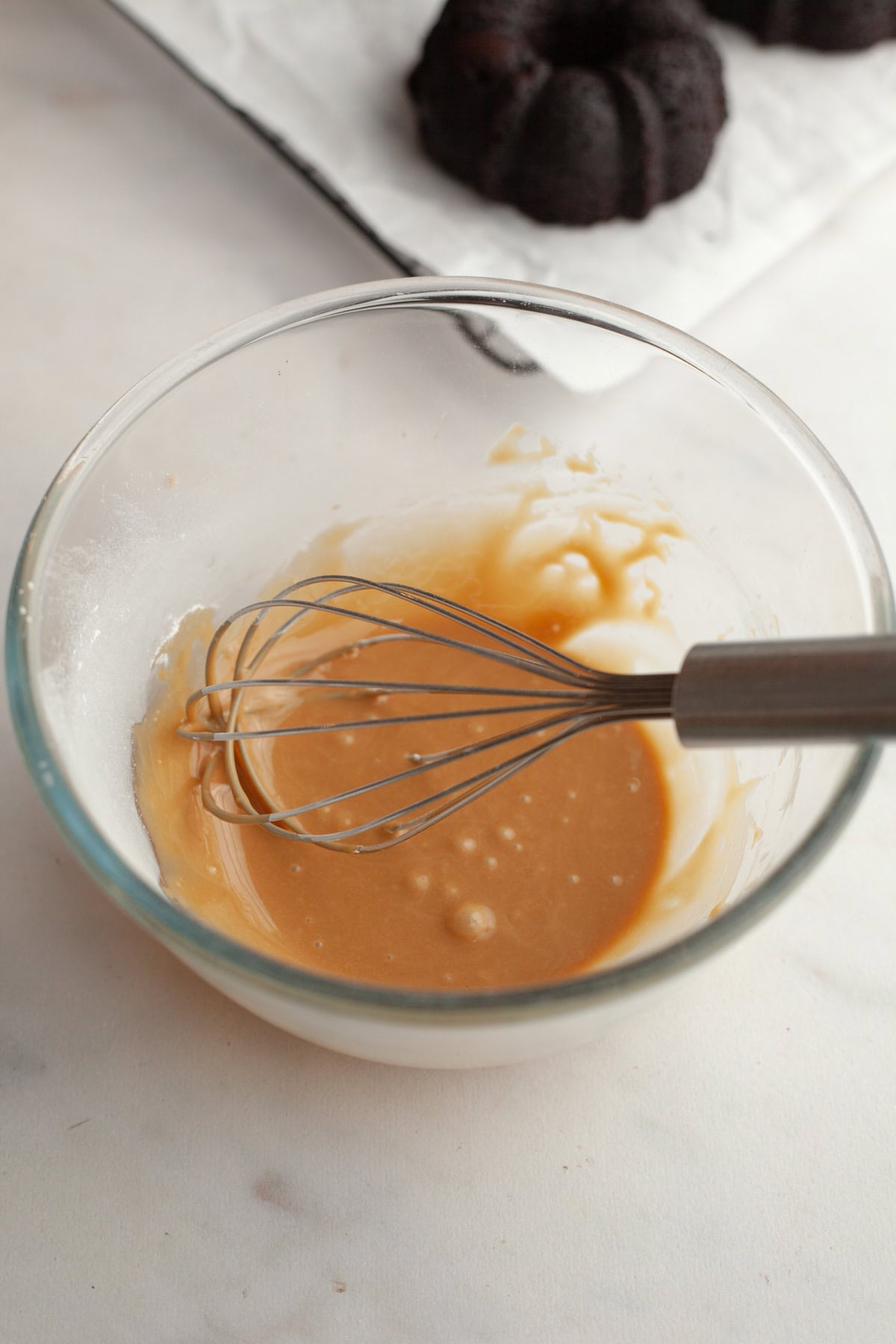 Espresso glaze in a glass bowl with a whisk.