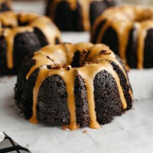 Mini chocolate bundt cakes with an espresso glaze on white parchment paper.