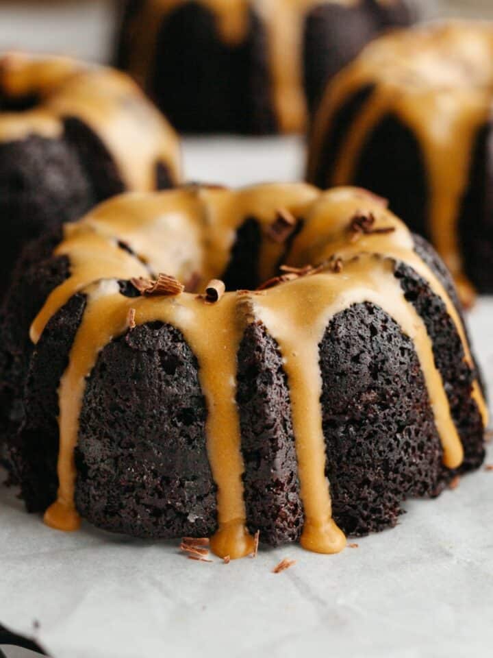 Mini chocolate bundt cakes with an espresso glaze on white parchment paper.