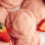 A close up of pink strawberry sugar cookies on parchment paper, there are a few sliced strawberries.