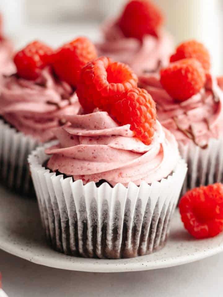 Close ups of chocolate cupcakes with raspberry buttercream, decorated with fresh raspberries.