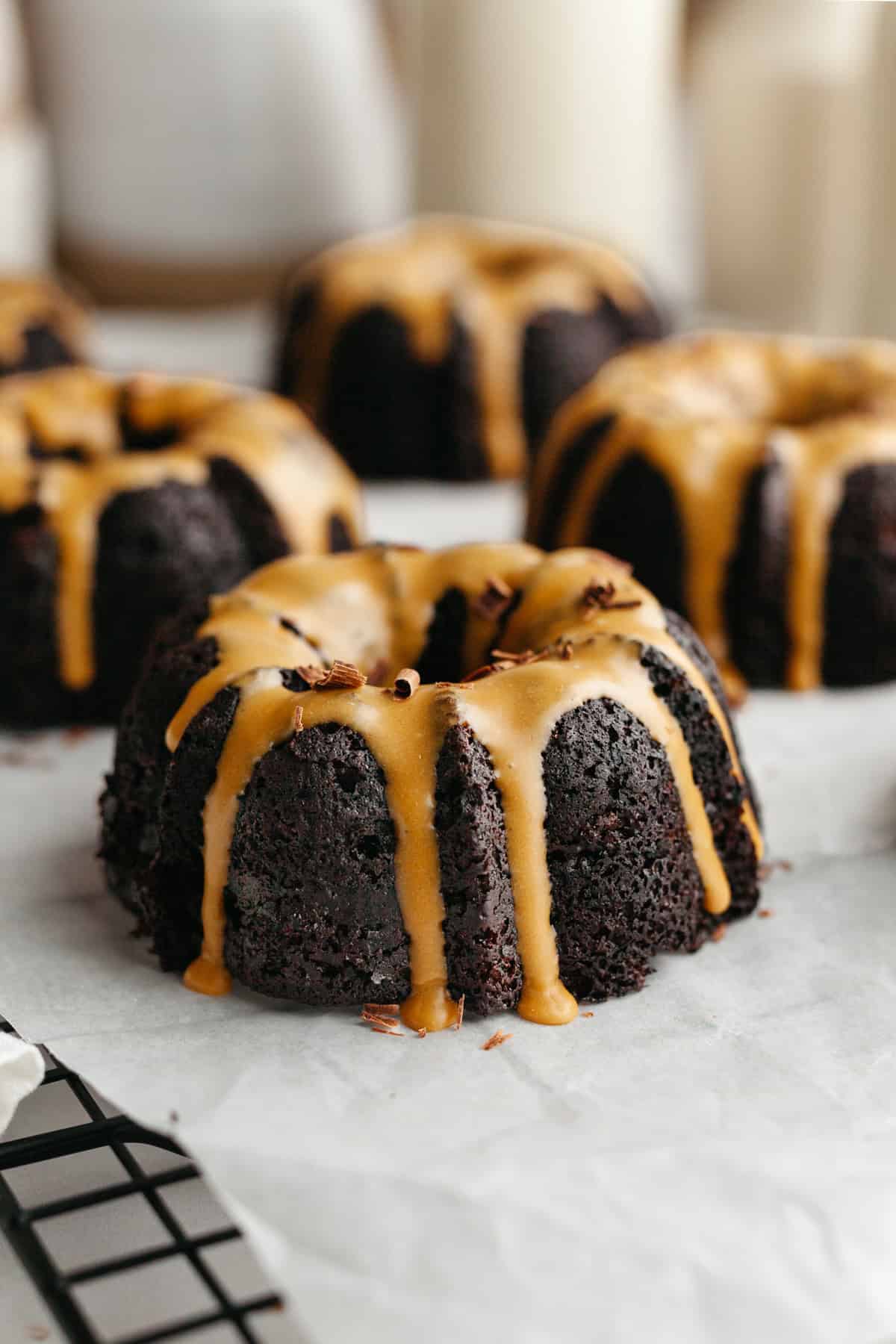 Mini chocolate bundt cakes with an espresso glaze on white parchment paper.