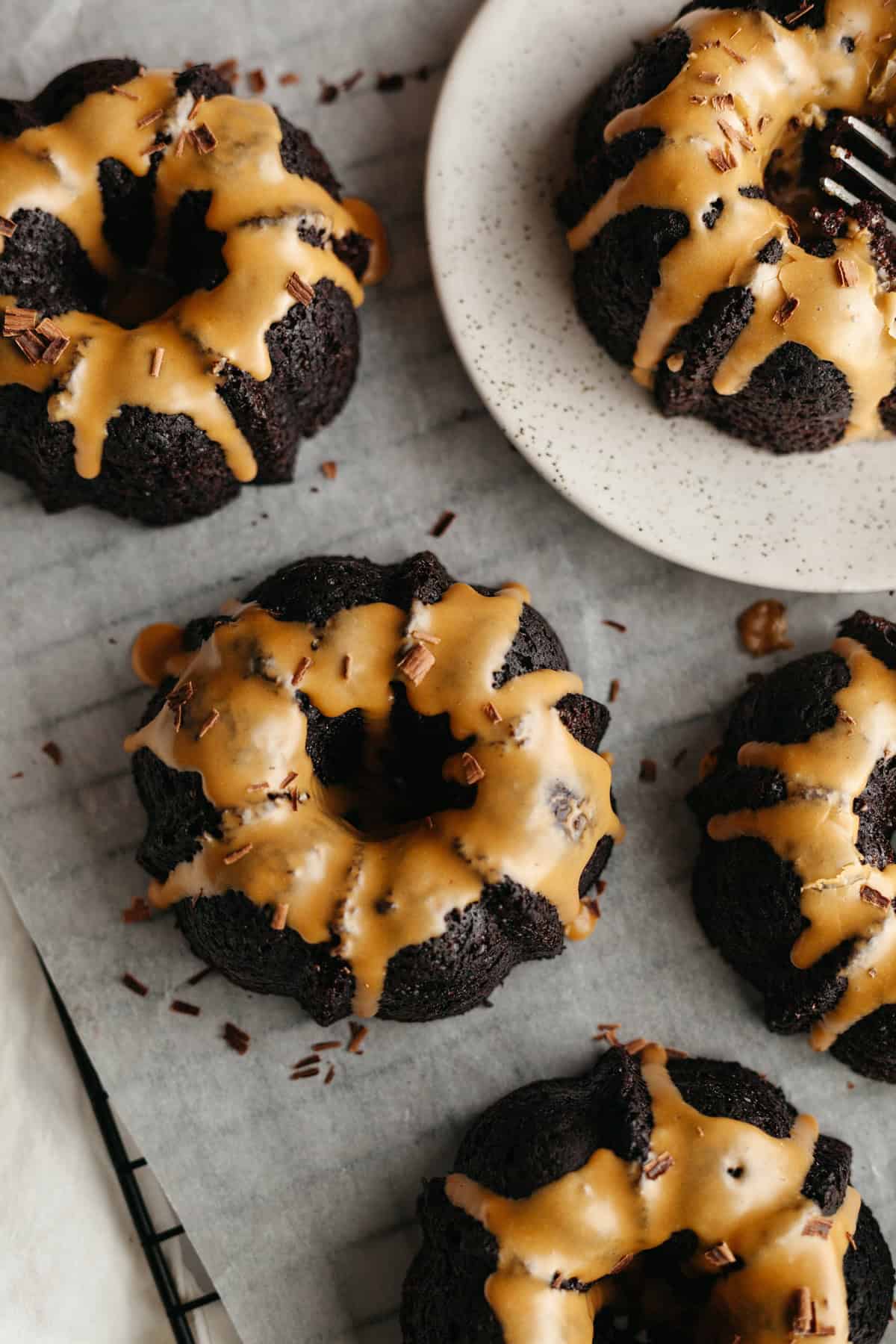 Mini chocolate bundt cakes with an espresso glaze on white parchment paper.