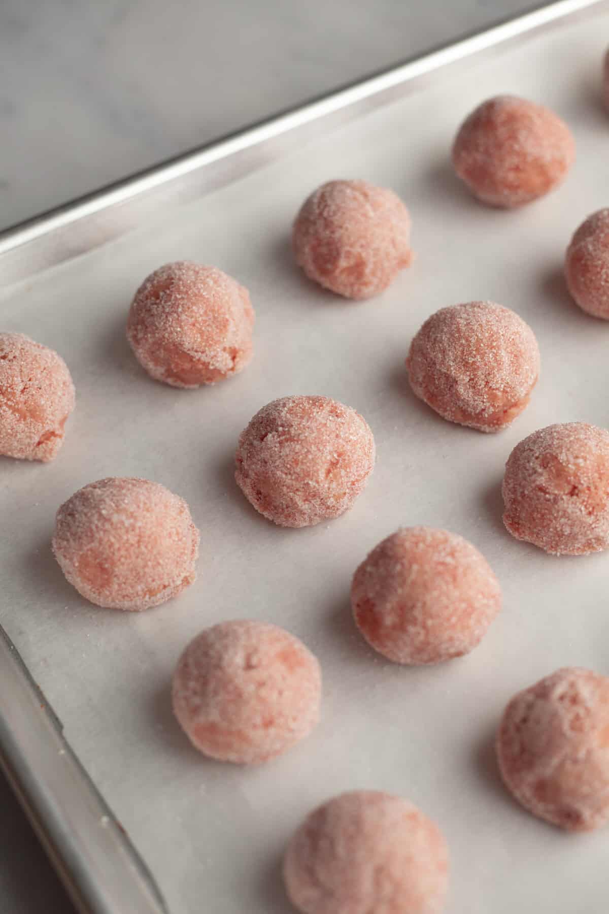 Strawberry sugar cookie dough balls on a parchment lined baking sheet.
