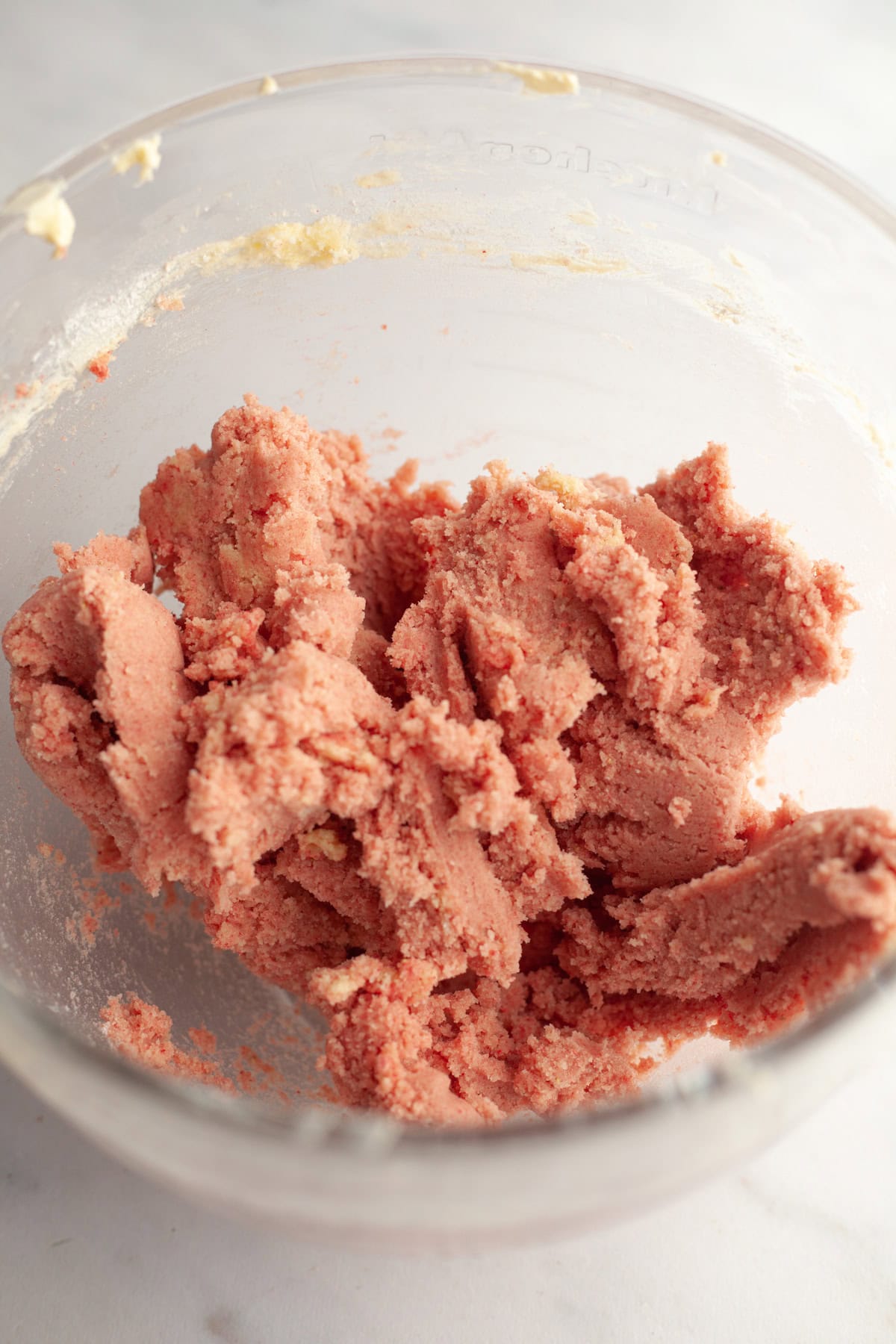 Pink sugar cookie dough in a glass mixing bowl.
